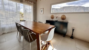 Een eetgedeelte met een houten tafel en stoelen, een zwarte kast en uitzicht op een bergachtig landschap door een raam.