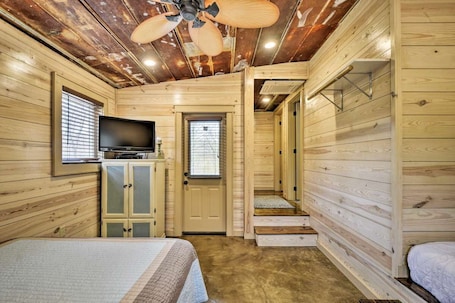 A wooden cabin room with a bed, a television, a cabinet, and a ceiling fan.