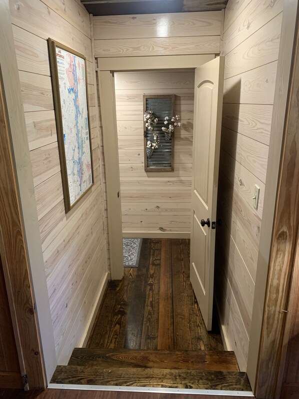 A narrow hallway with wooden walls and a wooden floor. A framed map is mounted on the left wall.