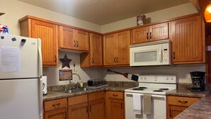 Una cocina con gabinetes de madera, un refrigerador blanco, un microondas, una estufa y una cafetera.