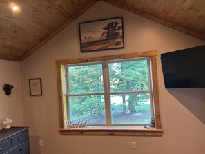 A room with a large window, a wooden ceiling, a framed picture, a TV, and a dresser. - Cozy Country farmhouse with Hot Tub (Meshoppen)