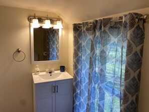 A bathroom with a white sink, a mirror with three lights, and a blue patterned shower curtain.