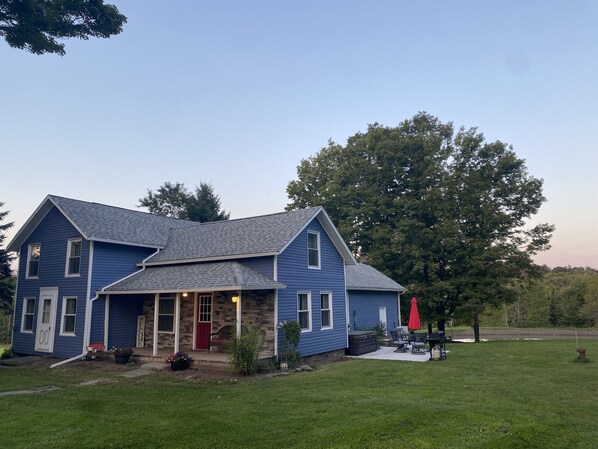 A two-story blue house with a front porch, a red door, and a patio with outdoor furniture.