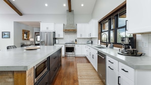 A modern kitchen with white cabinets, a large island, stainless steel appliances, and a wooden floor.