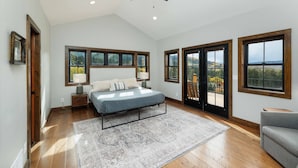 A bedroom with a bed, a ceiling fan, large windows, and a view of the outdoors.