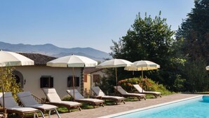 A poolside area with lounge chairs and umbrellas, a clear sky, and mountains in the background. - Villa Isabella by Interhome (Vicchio)