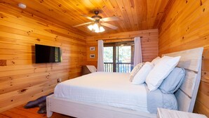 Ein Schlafzimmer einer Holzhütte mit Bett, Deckenventilator und an der Wand montiertem Fernseher.