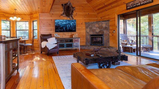 Ein Blockhaus-Interieur mit Kamin aus Stein, Holzmöbeln und einem an der Wand befestigten Fernseher.
