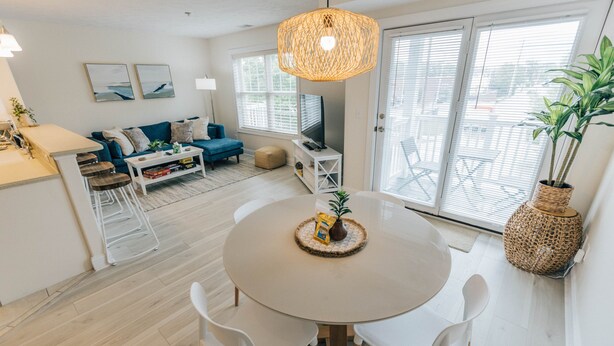 Un salon moderne avec une table ronde, des chaises blanches, un canapé et un téléviseur.