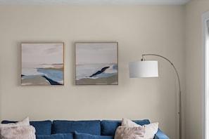 A room with a blue sofa, two abstract paintings, and a floor lamp.