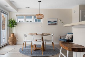 A dining area with a round table, chairs, a hanging light fixture, a potted plant, and a view of the outside through a window. - Relaxing Traverse City Condo near beaches and Town.  (Traverse City)