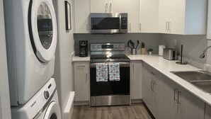 A compact kitchen with a washing machine, microwave, oven, and sink. - The Hamm Suite (Saskatoon)