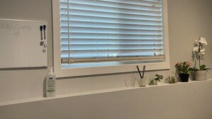 A room with a large window with blinds, a whiteboard with 'Welcome' written on it, and a shelf with plants and a bottle of hand sanitizer. - The Hamm Suite (Saskatoon)