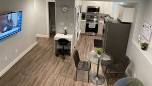 A modern kitchen with white cabinets, stainless steel appliances, and a dining area with a glass table and chairs. - The Hamm Suite (Saskatoon)