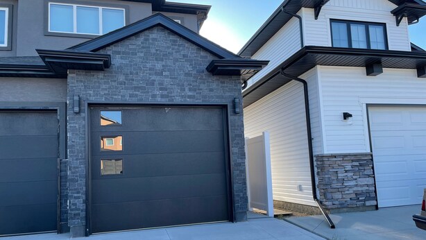 A residential garage with a dark gray door, a stone accent wall, and a white garage door. - The Hamm Suite (Saskatoon)