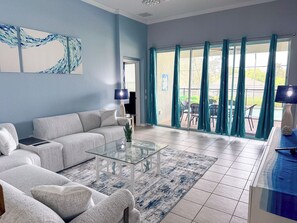 A living room with a sofa, coffee table, and a view of the outside through large windows.