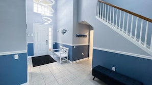 A hallway with a white bench, a door, and a staircase with a wooden handrail. - Under the Sea Villa – 3mi to Disney! Remodeled! 5 Bed&Bath, Private Pool/Spa! (Four Corners)