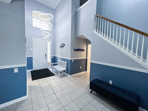 Ein Flur mit einer weißen Bank, einer Tür und einer Treppe mit einem Holzgeländer.