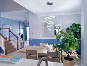 Et spiseområde med et træbord, stole, en lysekrone og en stor stueplante.