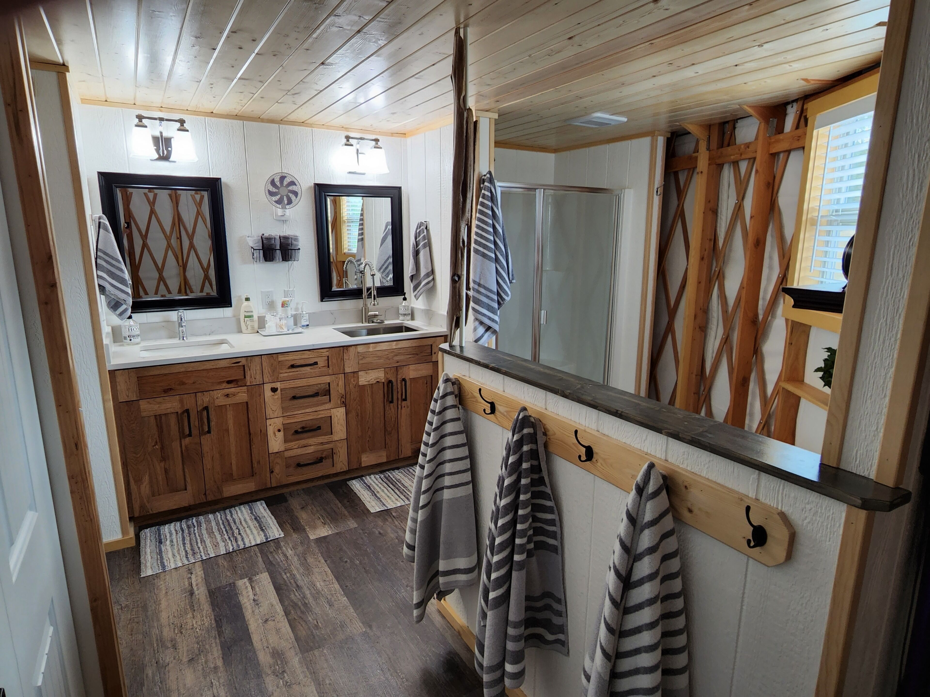 Un baño con armarios de madera, un espejo grande, un lavabo con tocador y toallas colgadas en ganchos.