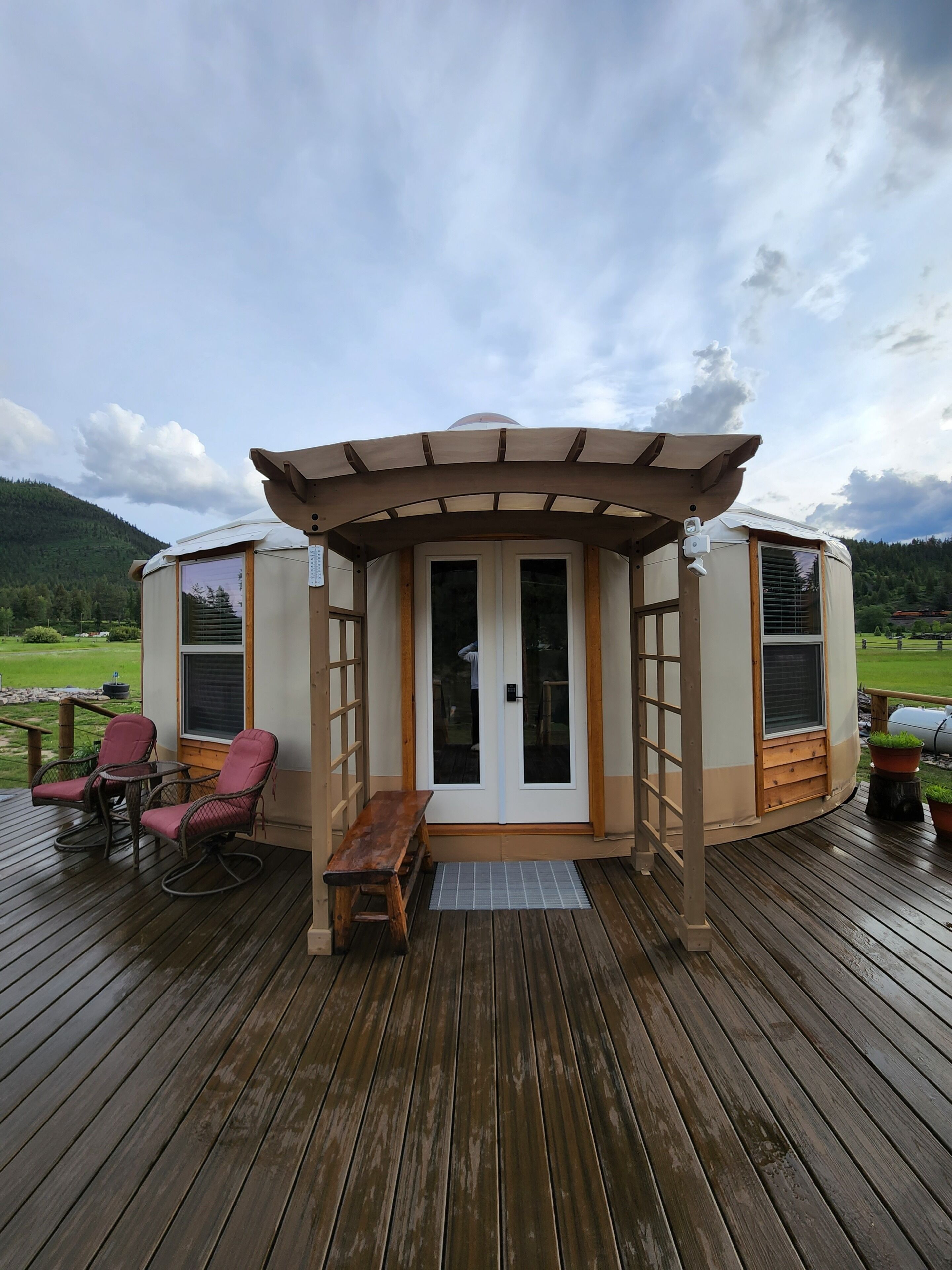 A yurt with a wooden deck, two rocking chairs, and a bench.