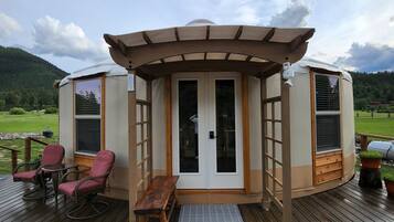 A yurt with a wooden deck, two rocking chairs, and a bench.