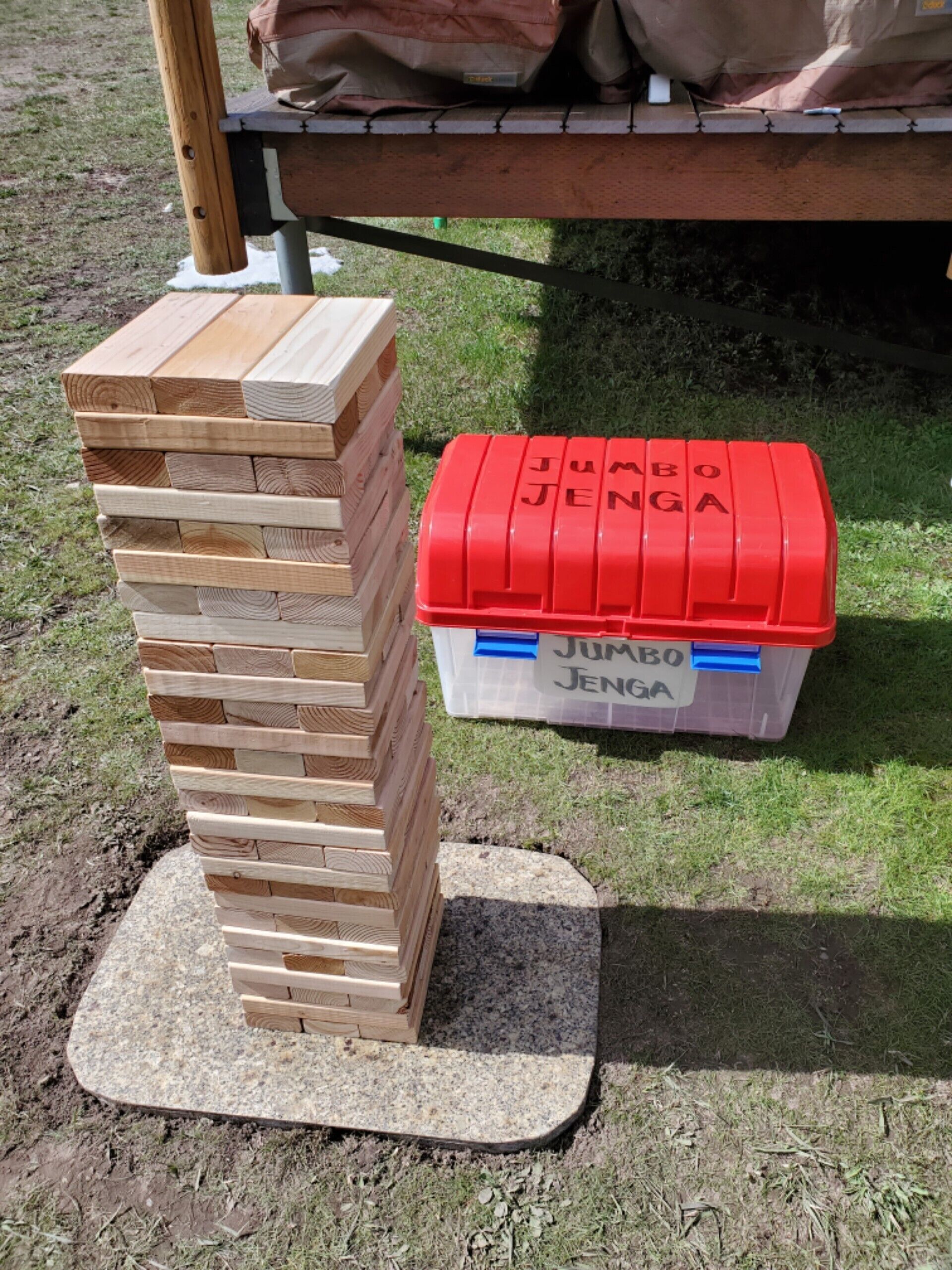 A wooden Jenga tower on a granite base outdoors.