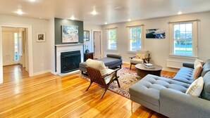 A spacious living room with hardwood floors, a fireplace, a grey sofa, a coffee table, and a patterned rug. - Historic Shoreline Home minutes to Stonington Village and Mystic! (Stonington)