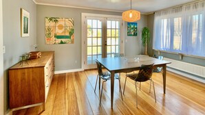 A dining area with a wooden table and chairs, a pendant light, and a view of the outdoors through a door. - Historic Shoreline Home minutes to Stonington Village and Mystic! (Stonington)