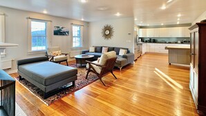 A spacious living area with a sofa, armchairs, and a coffee table. There is a kitchen in the background with white cabinets and a microwave. - Historic Shoreline Home minutes to Stonington Village and Mystic! (Stonington)