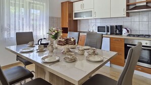 Cozinha moderna com armários brancos, uma mesa de jantar posta com pratos, xícaras e um bolo, e uma janela com cortinas leves.