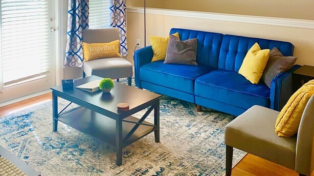 A living room with a blue sofa, a coffee table, a chair, and a ceiling fan. - Spacious 2bd apt in South Huntsville, close to Redstone Arsenal & downtown!! (Huntsville)