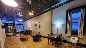 Une pièce chaleureuse avec un plancher en bois, un canapé, une table et des chaises. Il y a une fenêtre avec des rideaux, un ventilateur de plafond et un téléviseur fixé au mur.