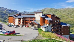 A modern hotel with multiple floors and a parking lot, set against a mountainous backdrop. - Nécou 505 by Interhome (Les Menuires)