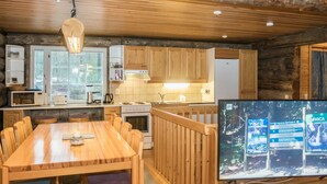 Une cuisine chaleureuse, aménagée dans le style d’un chalet, avec des meubles en bois, une table à manger et un téléviseur diffusant des brochures de voyage.