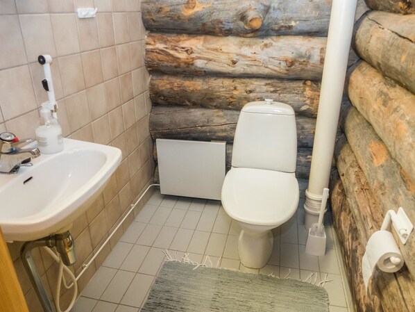 Un baño con lavamanos, inodoro y pared de troncos.