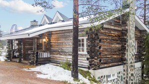 Une cabane rustique en rondins de bois, dotée d’un porche, d’une cheminée et d’un mur en pierre.