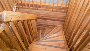 Un escalier en colimaçon en bois, doté d’une rampe métallique et d’une main courante en bois.
