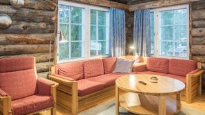 L’intérieur d’une cabane en rondins, avec un canapé rouge, une chaise en bois et une table ronde.
