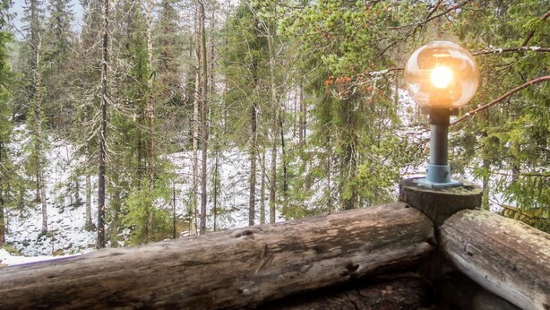 Une cabane avec une balustrade en bois, une porte en verre et une vue sur une forêt dont le sol est recouvert de neige.