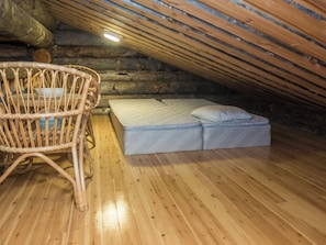 A cozy attic bedroom with a wooden floor, a wicker chair, and a simple bed.