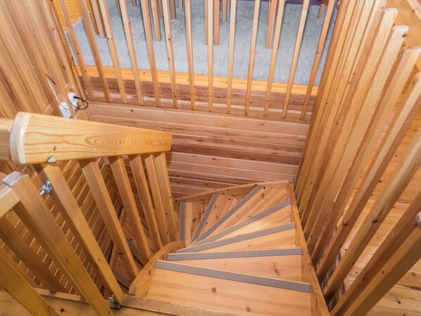 A wooden spiral staircase with metal handrails, leading to an upper level.