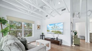 A modern living room with a large window, a flat-screen TV, and a minimalist design. - 🌴Beachside Escape Private Modern Heated Pool - Vacation Getaway Gulf Shores🌴 (Gulf Shores)