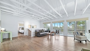 A spacious living room with a wooden floor, a grey sofa, a wooden chair, and a white armchair. There is a small table with a lamp and a painting on the wall. - 🌴Beachside Escape Private Modern Heated Pool - Vacation Getaway Gulf Shores🌴 (Gulf Shores)