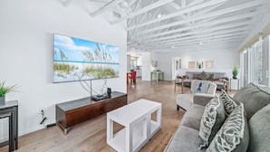 A modern living room with a large flat-screen TV, wooden flooring, a white coffee table, and a grey sofa with patterned cushions. - 🌴Beachside Escape Private Modern Heated Pool - Vacation Getaway Gulf Shores🌴 (Gulf Shores)