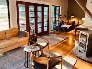 A cozy living room with a leather sofa, a wooden chair, a small table with a book, a fireplace, and a telescope.