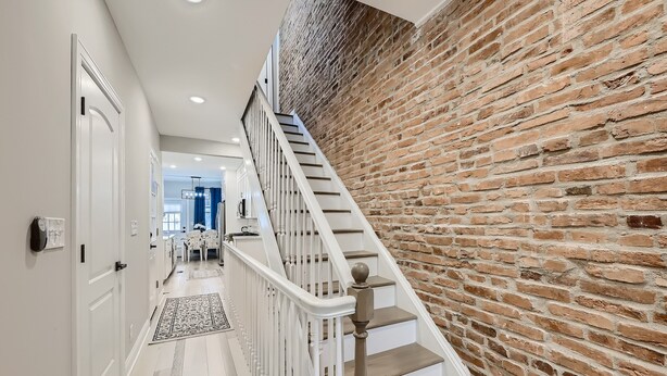Un escalier avec des rampes blanches et des marches en bois menant à une pièce dont un des murs est en briques.