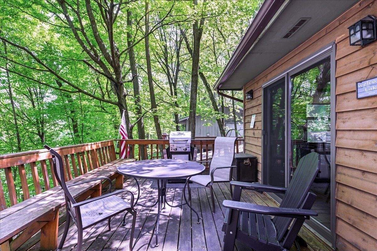Une terrasse en bois avec une table et des chaises, un barbecue et un panneau indiquant : « Bienvenue au bord du lac ».