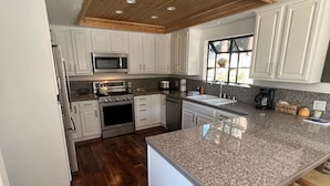 Una cocina moderna con armarios blancos, encimera de granito y techo de madera.