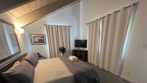 Una habitación de hotel con cama, televisión, ventilador y cortinas.